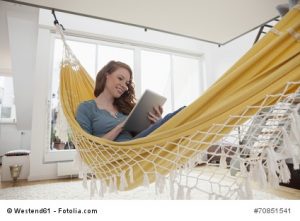 Lächelnde Frau entspannt mit Tablet-Computer in einer Hängematte in ihrer Wohnung