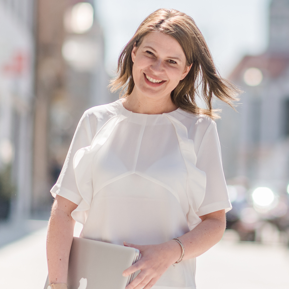 Bernadette hält ihren Laptop in der Hand und lächelt in die Kamera